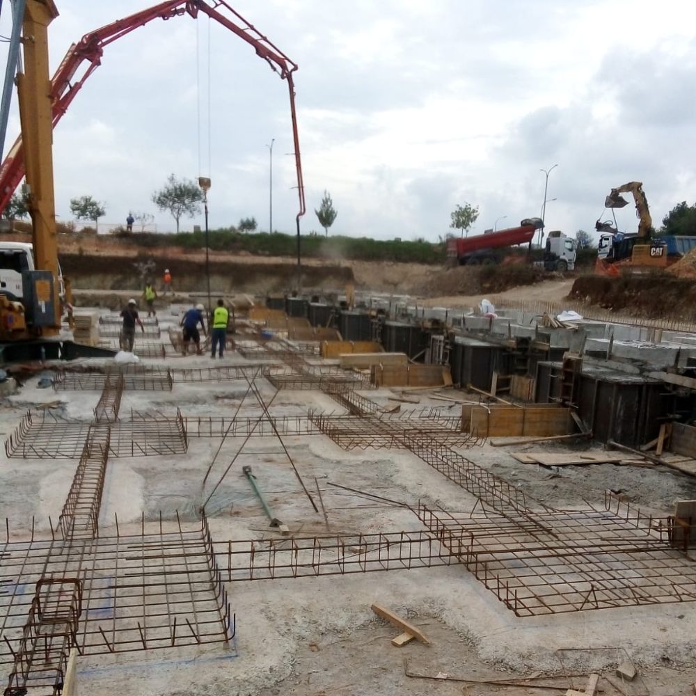Trabajadores realizando encofrado y cimentación en la construcción de la nave de distribución de Bebidas Arta, con maquinaria pesada y estructuras de soporte en obra. Proyecto desarrollado por Estructuras Mañez.