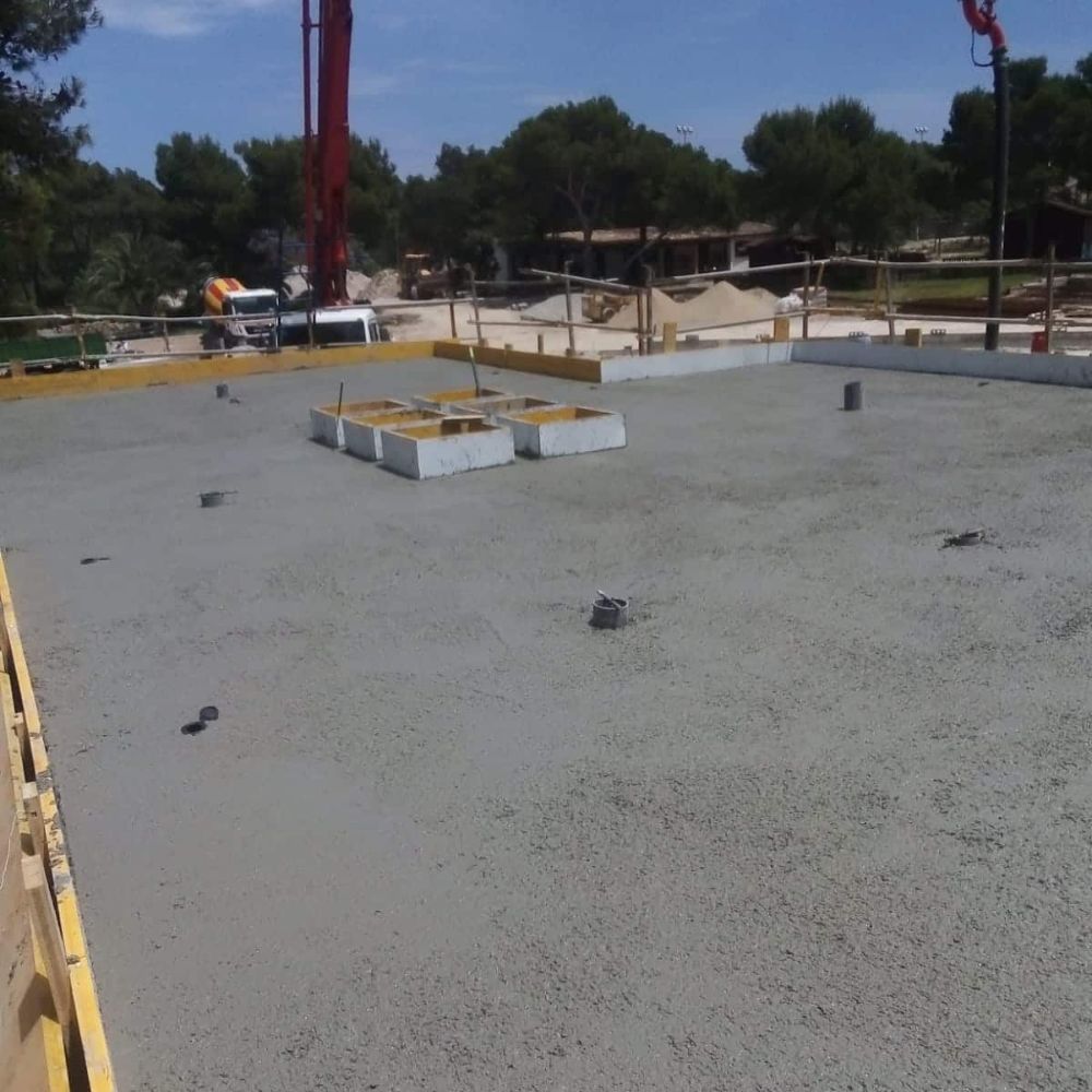 Proceso de vertido de hormigón en la losa de cimentación en la construcción del hotel Cala Barca, con maquinaria y encofrado en el sitio